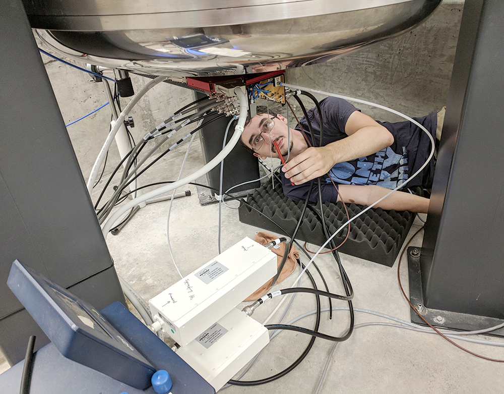 A man lying down on a foam pad underneat an NMR magnet